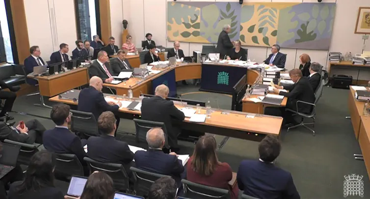 Boris Johnson sitting at a table facing a committee of MPs, sitting in a semi circle.