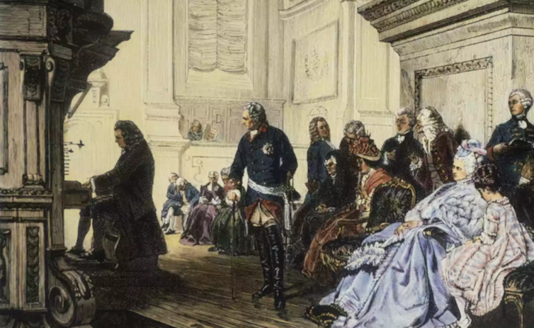 Un hombre toca el órgano de espaldas a un grupo de gente sentada, atendiendo.