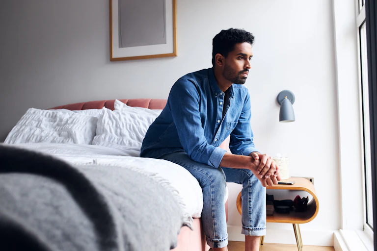 A man sits on his bed, appears despondent.