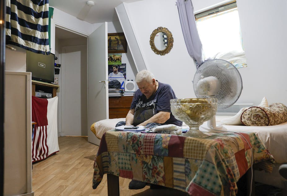 vieil homme assis sur son lit à côté d'un ventilateur