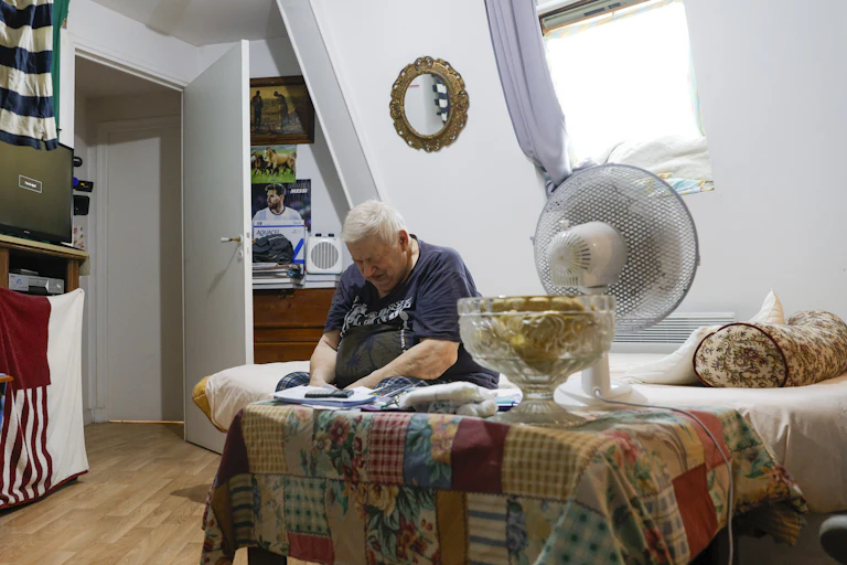 vieil homme assis sur son lit à côté d'un ventilateur