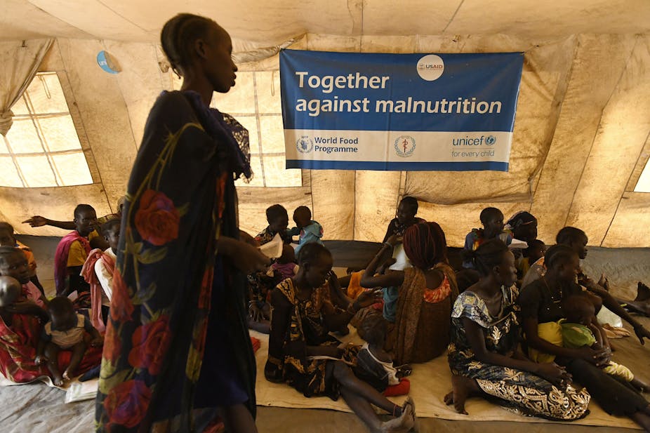 A woman walks past a banner that reads "Together against malnutrition" while other women sit on the floor of a large tent