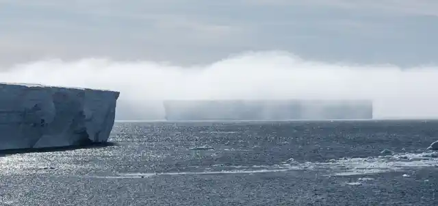 A blanket of fog draped over two vast icebergs.