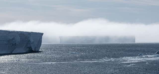 A blanket of fog draped over two vast icebergs.