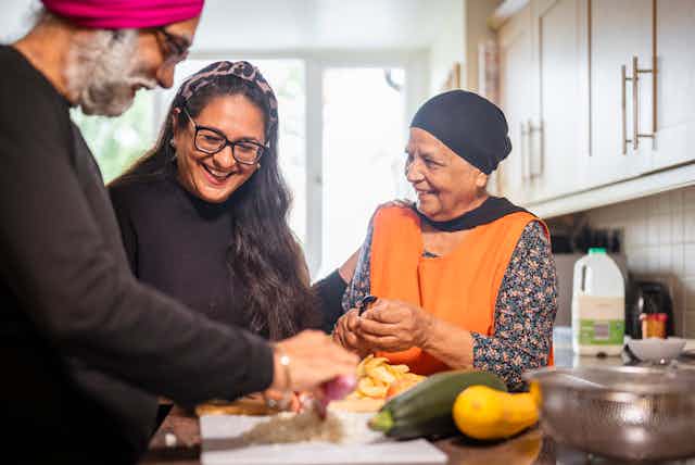 A young South Asian woman helps an older Sikh couple prepare food in a home kitchen