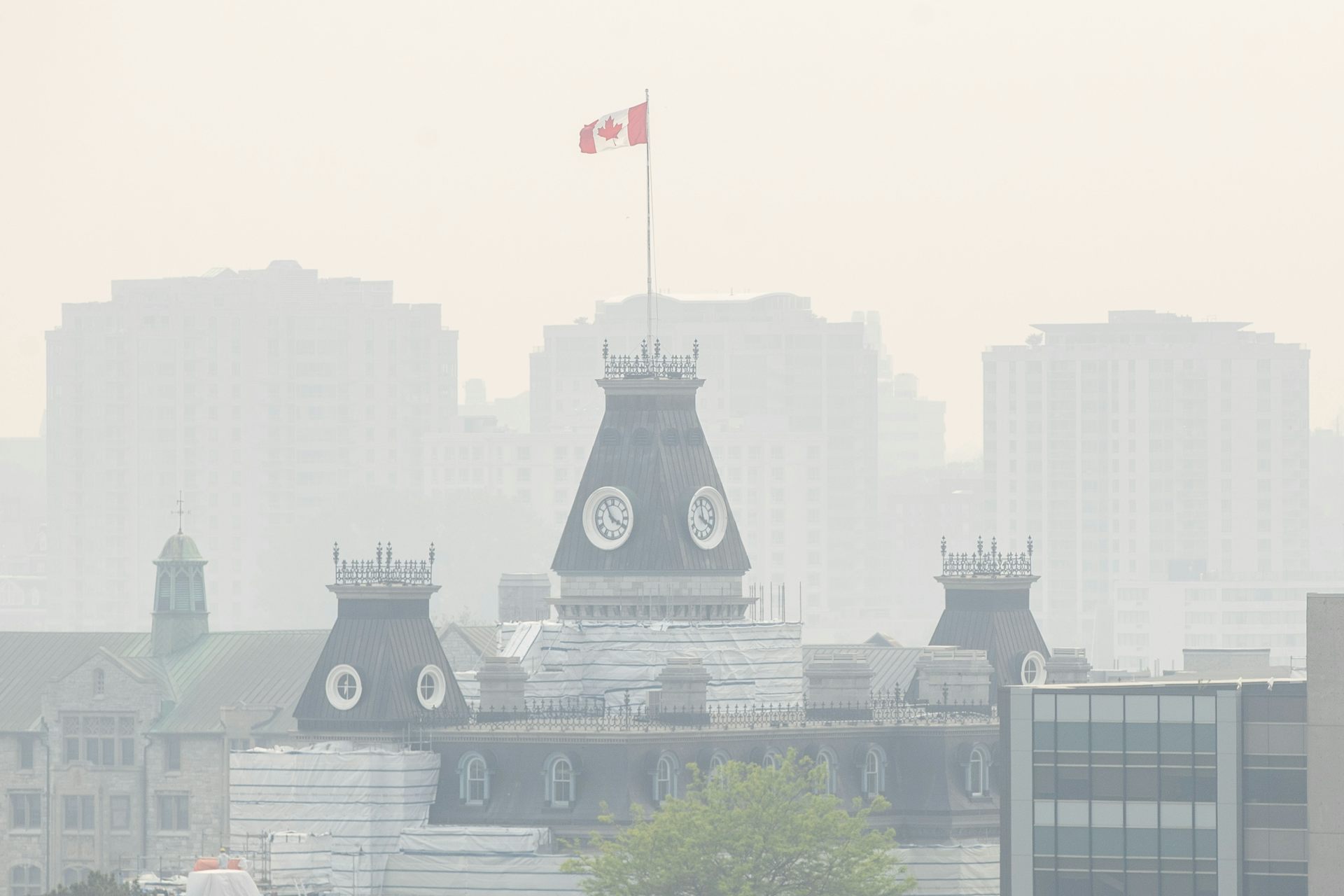 Peaked buildings, one with a Canadian flag flying over it, in a smoky haze.