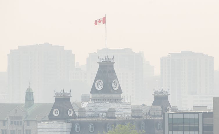 Peaked buildings, one with a Canadian flag flying over it, in a smoky haze.