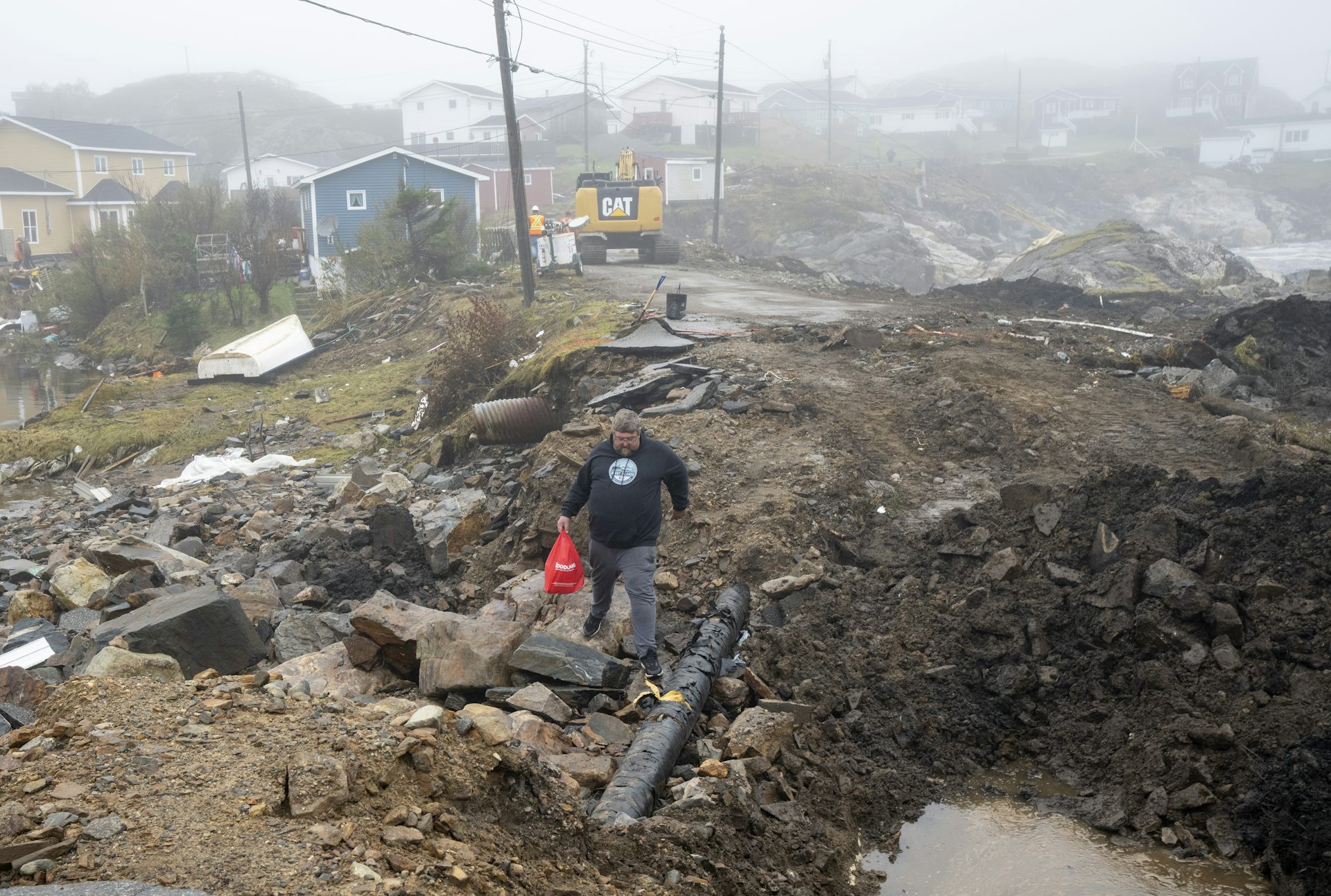A man carries a bag of groceries over a mound of debris and rubbage.