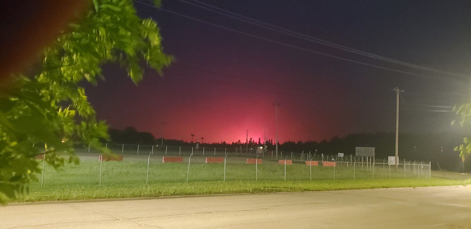 The red glow of a forest forest is seen on the horizon, with trees and a field in the foreground.
