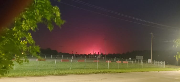 The red glow of a forest forest is seen on the horizon, with trees and a field in the foreground.