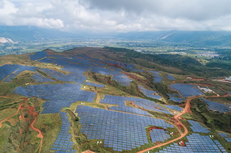 An aerial photograph of a photovoltaic power plant on a lush hillside.