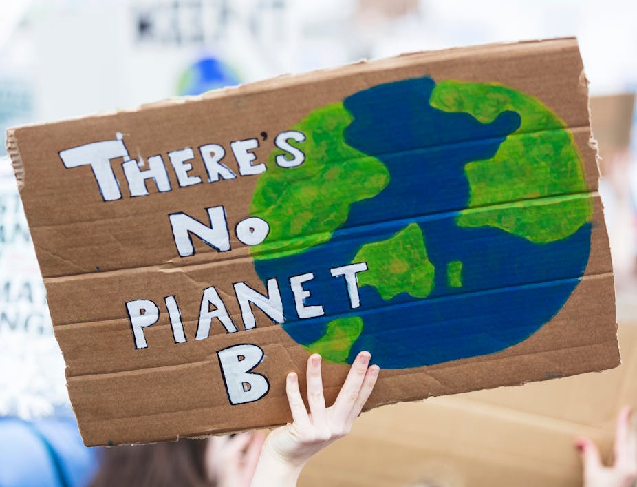 A person holding up a cardboard sign reading: 'There's No Planet B'.
