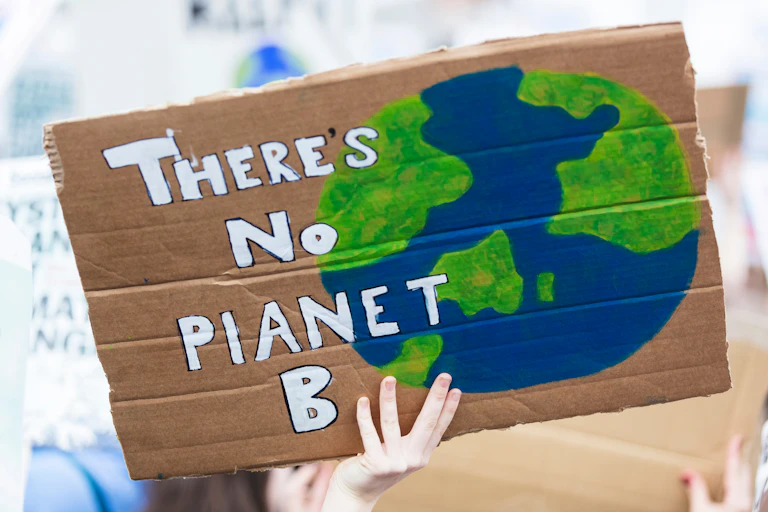 A person holding up a cardboard sign reading: 'There's No Planet B'.