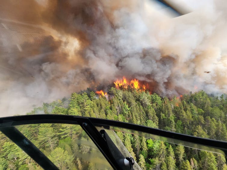 The orange flames of a wildfire and billowing brown smoke are seen from above.