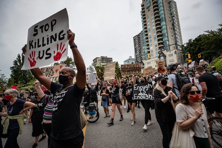 People seen marching in the streets, with one person holding a sign that says 'stop killing us.'