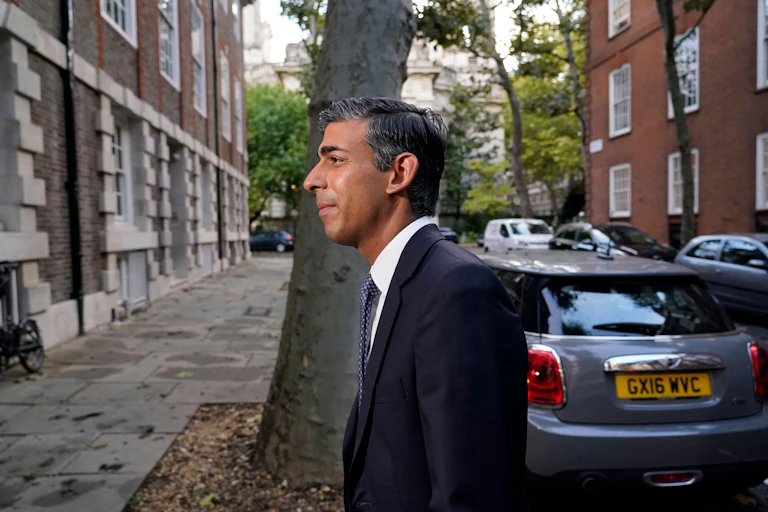 Rishi Sunak walking on a street in front of a tree.