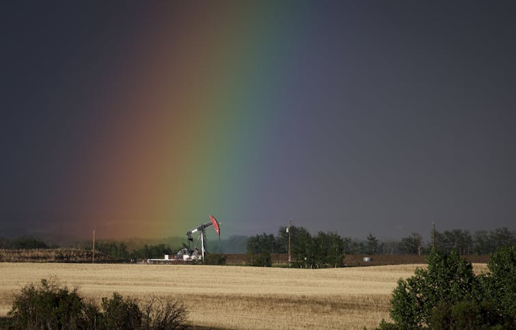 A rainbow ends near a working pumpjack.