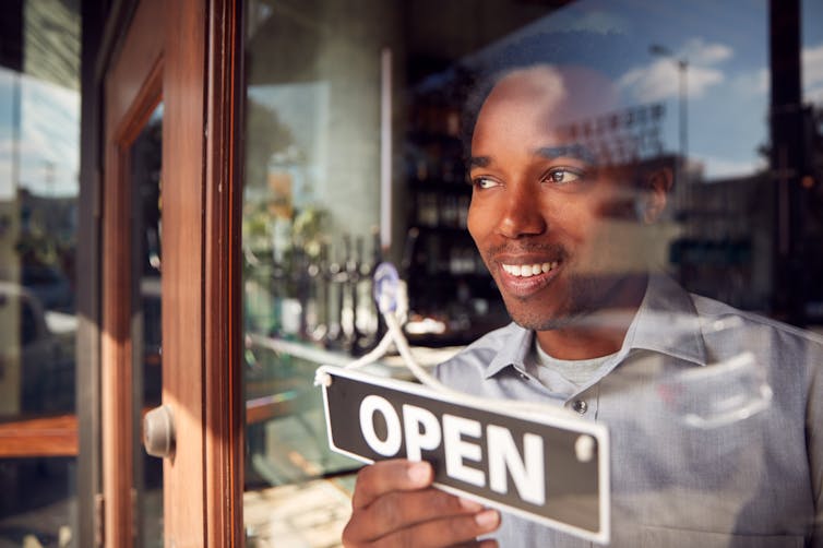 Personne dans la fenêtre d'un commerce qui tient une enseigne lisant "Open"