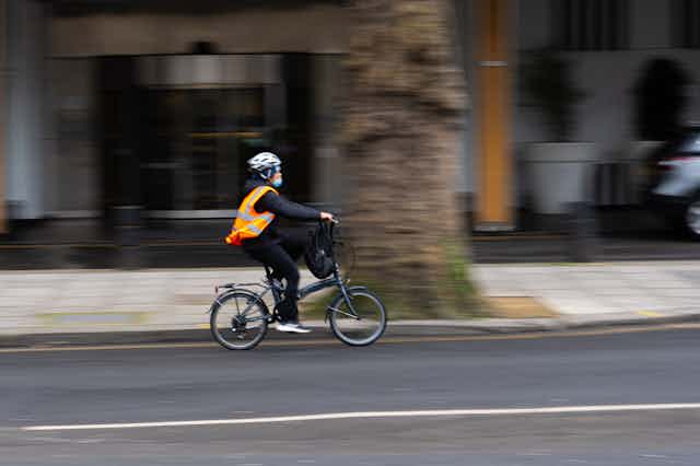 Man wearing a safety vest and helmet rides a bike along a city road