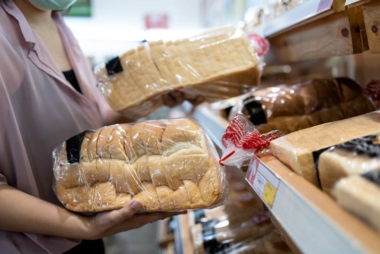 A woman holds two loaves of supermarket bread in her hands.