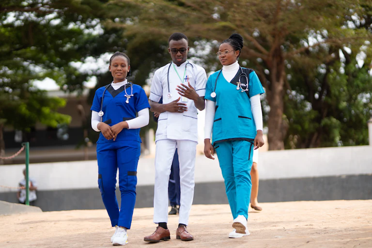 Two women dressed in blue medical scrubs and a man in white scrubs walking, they all have stethoscopes around their necks.