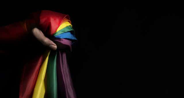 A person's hand clutched around a pride flag against a dark background
