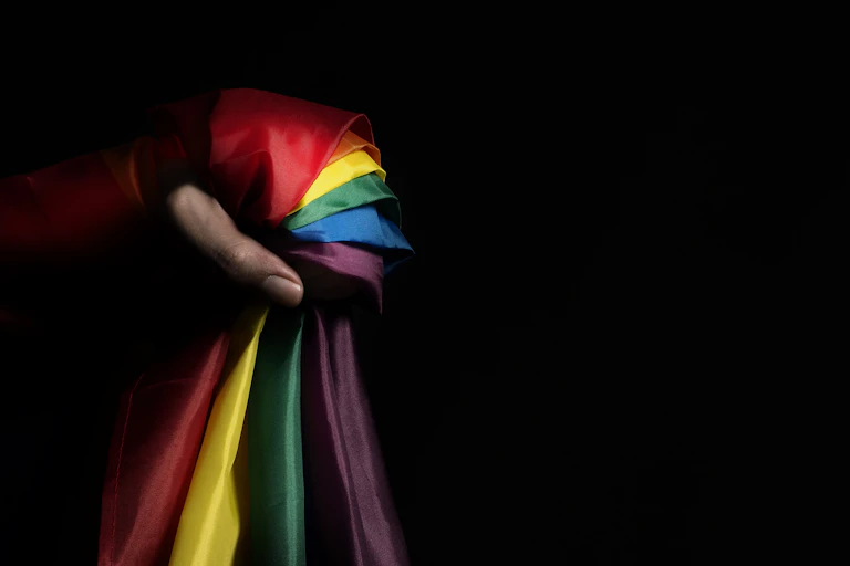 A person's hand clutched around a pride flag against a dark background