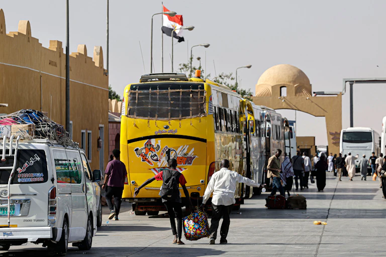 People carrying bags and walking towards parked buses.