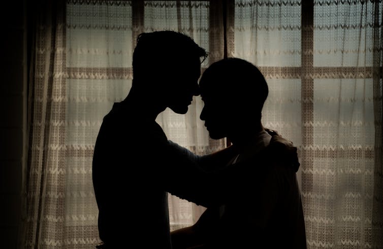 Silhouette of two men embracing in front of curtains in a room