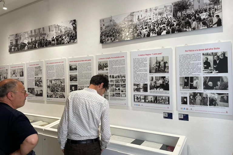 Una habitación con una exposición mural con fotografía y texto y mesas sobre las que se encuentran objetos.
