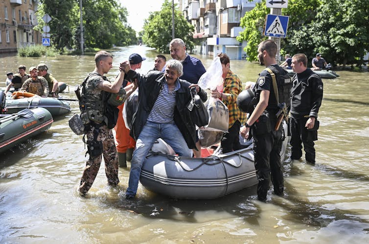A group of men dressed in military fatigues help get off a small boat on a street that had been flooded.