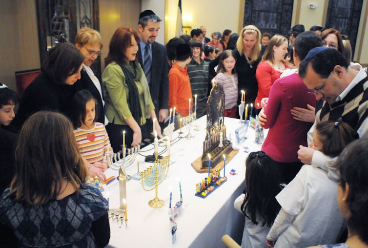 A group of people gather around a table with several menorahs on it.