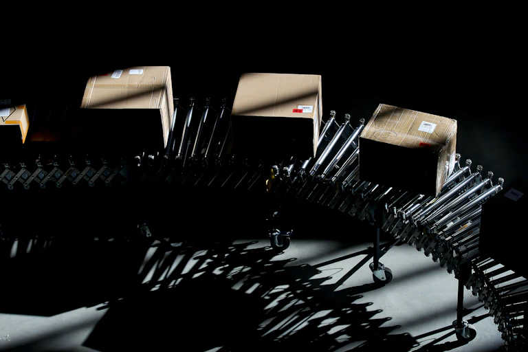 Four odd-sized boxes without logos roll down an assembly line inside an Amazon logistics center.
