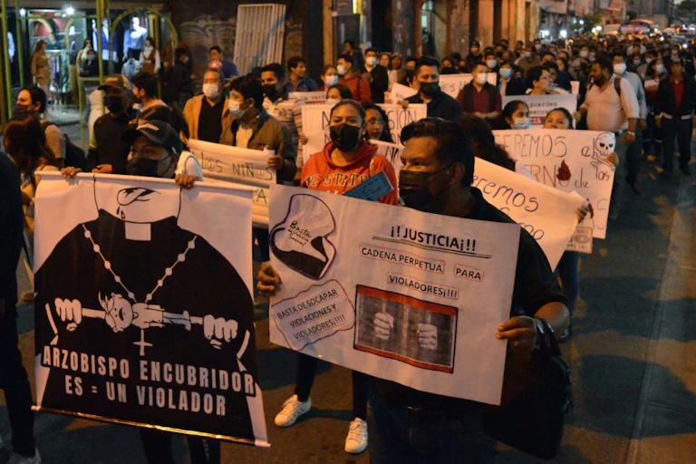 Rows of people walking in an evening protest and holding white handmade signs.