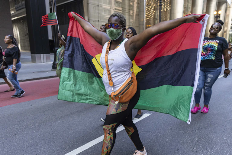 A woman seen holding a red, black and green striped flag with her arms outstretched at a rally.