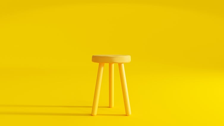 Yellow three-legged stool against yellow background