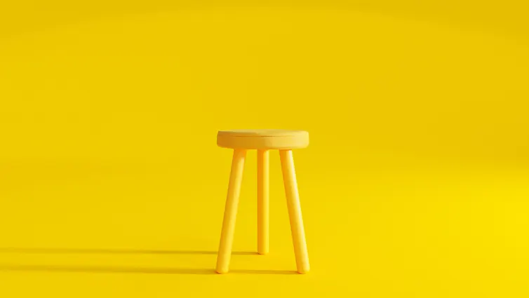 Yellow three-legged stool against yellow background