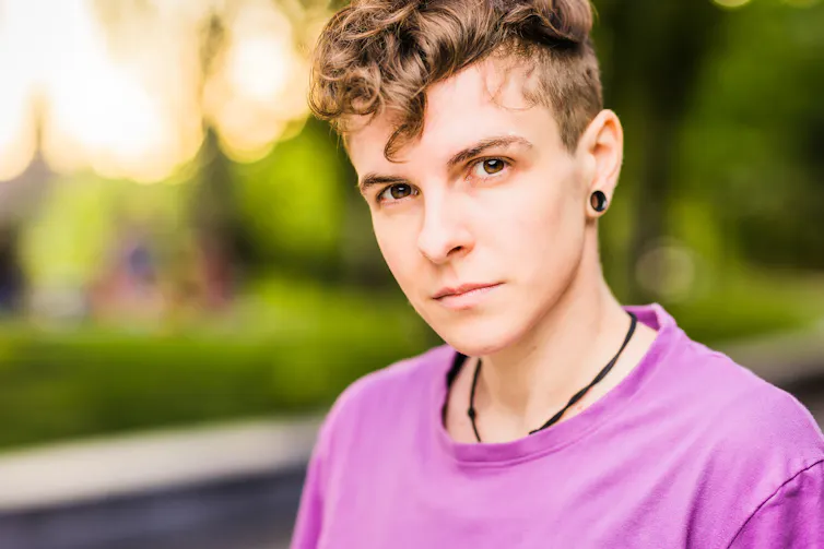 A person in a purple T-shirt outdoors, looking at the camera,