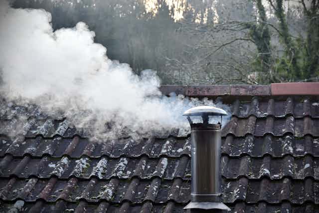 Smoke from a wood heater comes out of a rooftop chimney