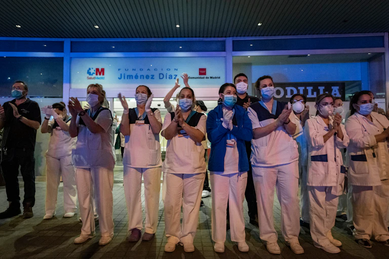 Muchos sanitarios aplaudiendo en la parte exterior de un hospital.