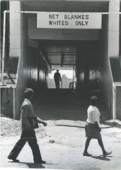Two people of colour pass an entrance to a public facility that has a large sign above it reading