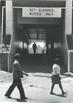 Two people of colour pass an entrance to a public facility that has a large sign above it reading