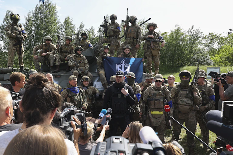 A group of soldiers holding up flags talk to the press.