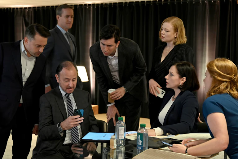 A group of business people gathered around looking at someone's phone screen.