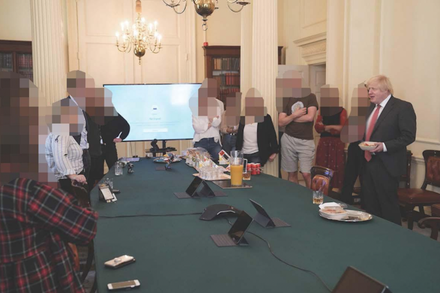 Boris Johnson standing with people whose faces have been pixellated. They are in a government room around a table with refreshments on it.   