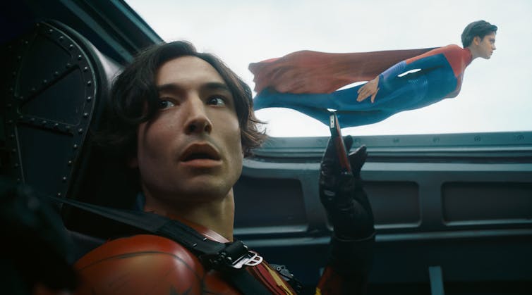 Ezra Miller as The Flash pointing in shock at Supergirl flying alongside the plane he's in.
