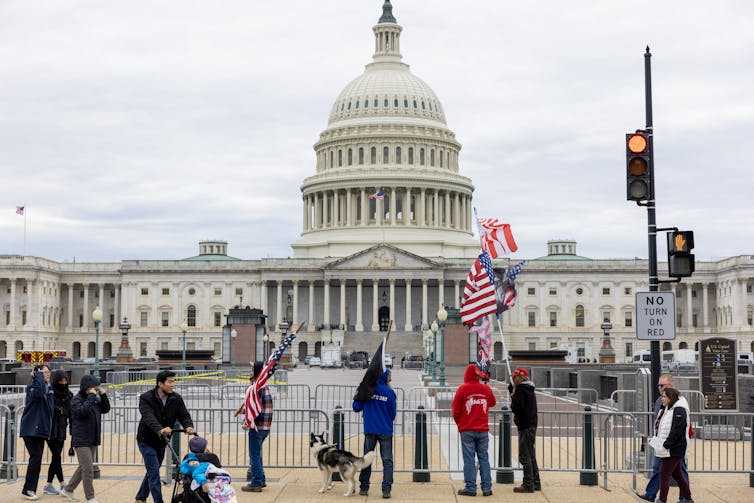 A few people holding American flags stand outside of the U.S. Capitol building in Washington, D.C., on a gray day.