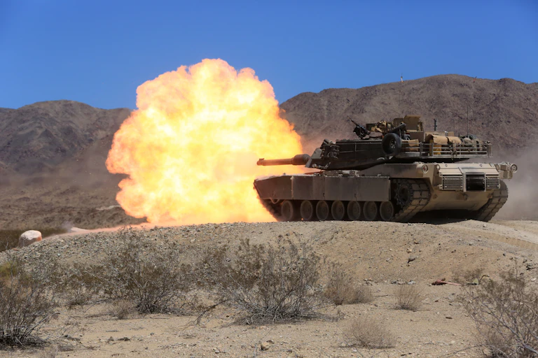 A tank on a sandy range with a large explosion coming from its main gun