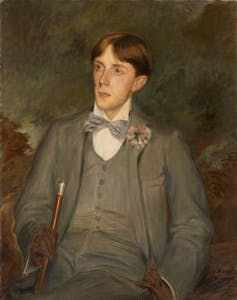 Aubrey Beardsley in a grey suit with button hole flower.