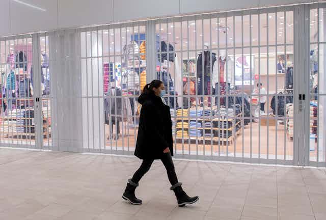A woman in a medical mask walks past a closed store in a mall
